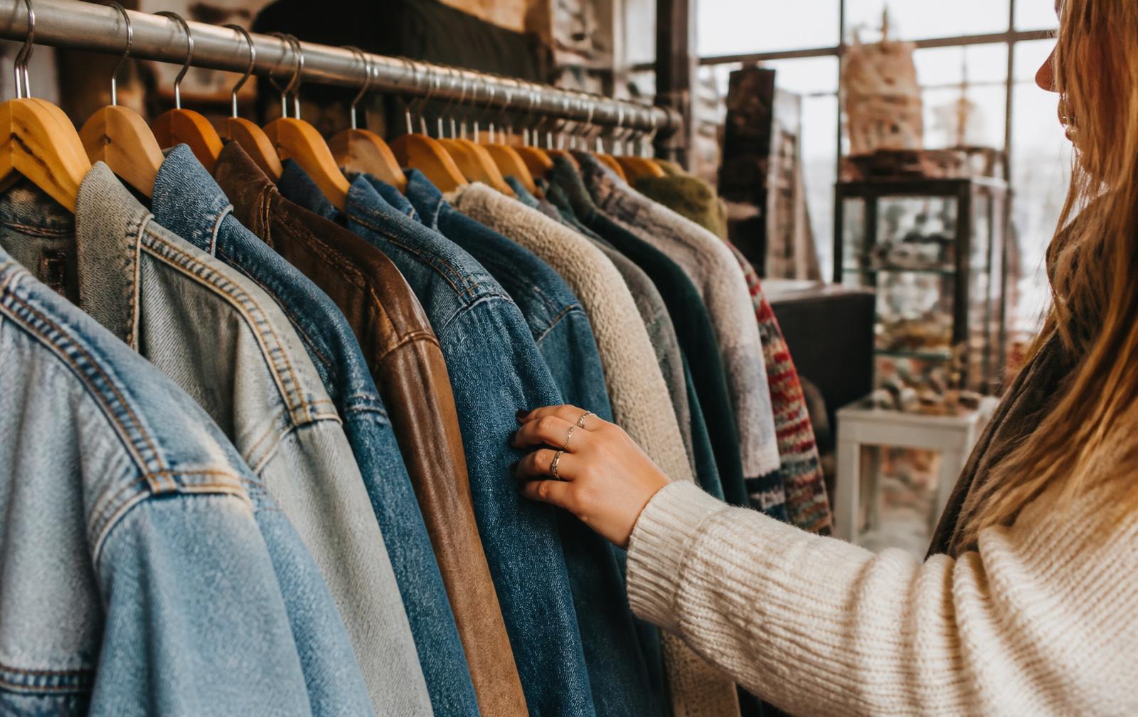 Percha con denim, cuero y punto de segunda mano en una tienda de ropa vintage